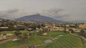 Ein Golfplatz mit Clubhaus, Palmen und einem Berg im Hintergrund.