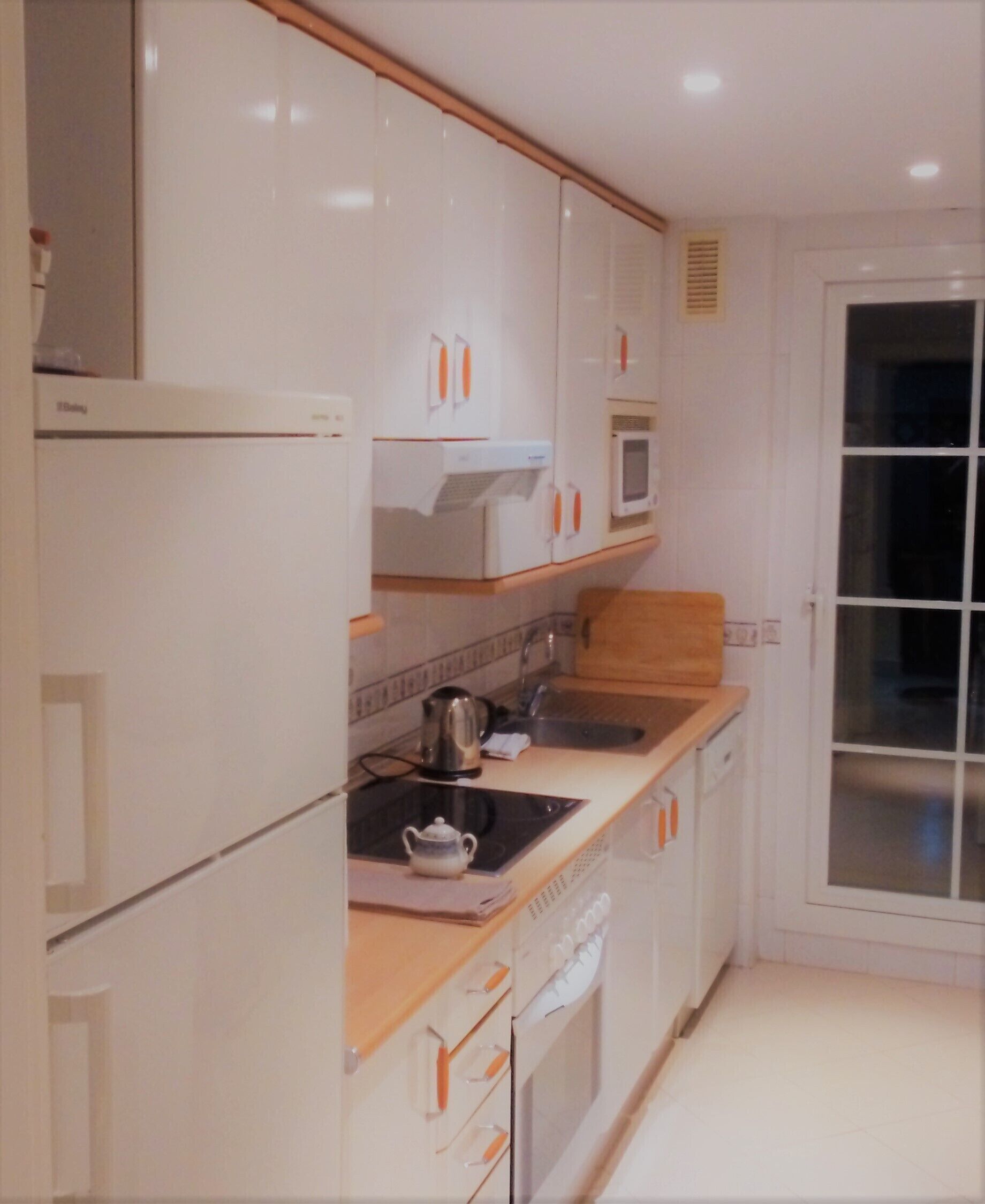 Une cuisine moderne avec des meubles blancs, un four à micro-ondes, une bouilloire et un lave-vaisselle.