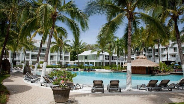 A resort pool area with palm trees, lounge chairs, and a thatched-roof hut. - 5313 Coral Suite The Beach Club (Palm Cove)