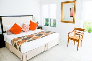 Ein ordentlich bezogenes Bett mit einer gemusterten Tagesdecke, ein Holzhocker und ein großer Spiegel an der Wand.