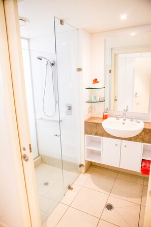 Ein modernes Badezimmer mit einer Duschkabine aus Glas, einem weißen Waschbecken und einem Spiegel darüber.