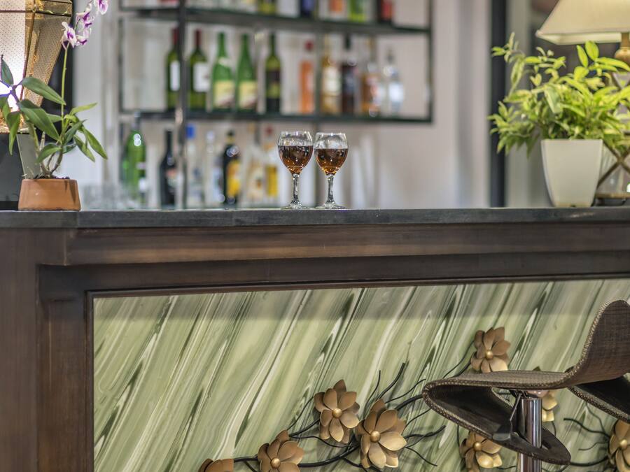 Uma área de bar com bancada de mármore, dois copos com líquido âmbar e um arranjo floral decorativo.