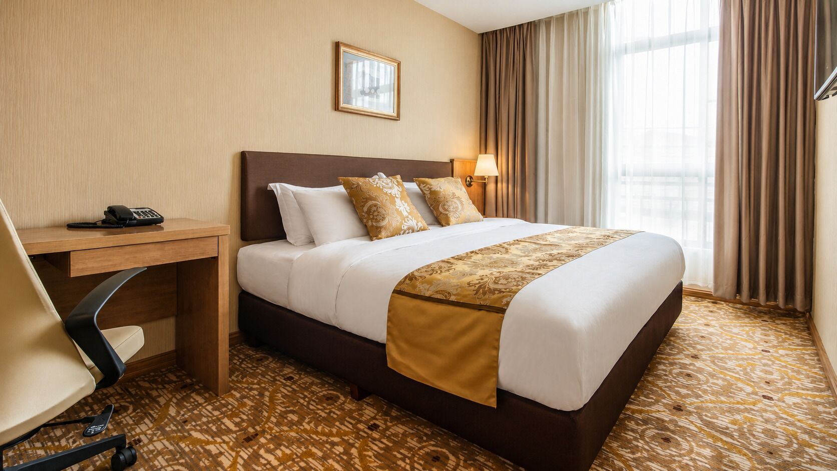 A hotel room with a bed, desk, chair, and a telephone.