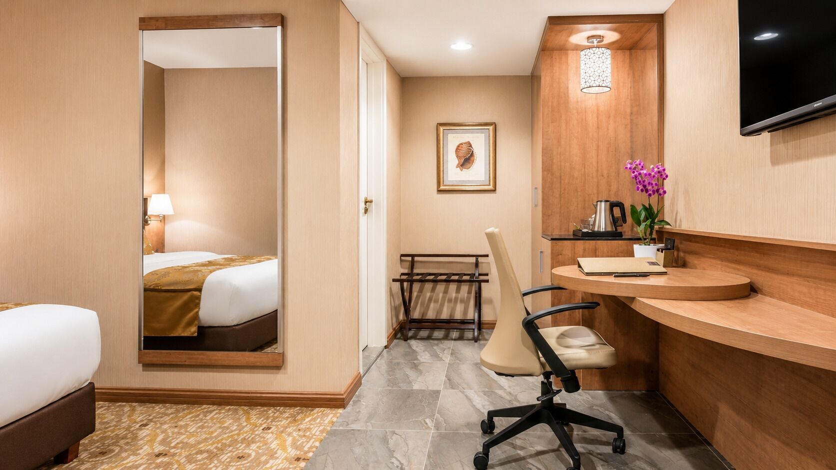 A hotel room with a bed, a desk, a chair, a mirror, a television, and a framed picture on the wall.