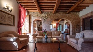 Un salón acogedor con un arco de piedra, vigas de madera y una mesa de centro de vidrio con un jarrón.