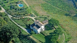 Vista aérea de una propiedad que incluye un edificio blanco grande, una piscina y amplios campos de viñedos.