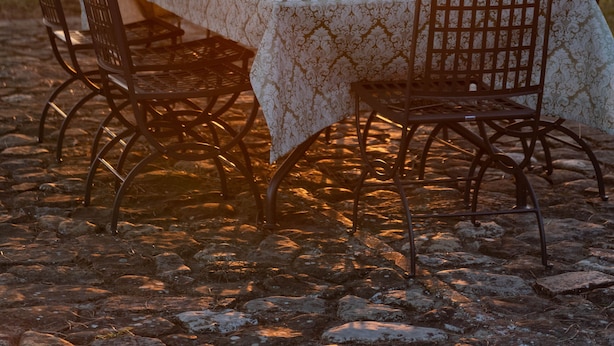 Mesa al aire libre con mantel estampado, sillas de metal y botellas de vino.