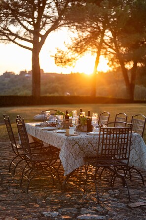 A table set outdoors with a patterned tablecloth, metal chairs, and wine bottles.
