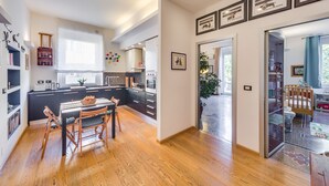 A modern kitchen with dark cabinetry, a wooden dining table, and a view into the living area.