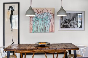 Un comedor con una mesa de madera, dos lámparas colgantes y tres obras de arte enmarcadas en la pared.
