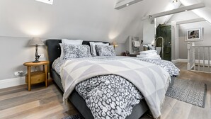 A bedroom with a large bed, a bedside table, a lamp, and a walk-in closet.