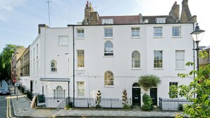 A white two-story building with a black iron fence, a black door, and a small garden area.