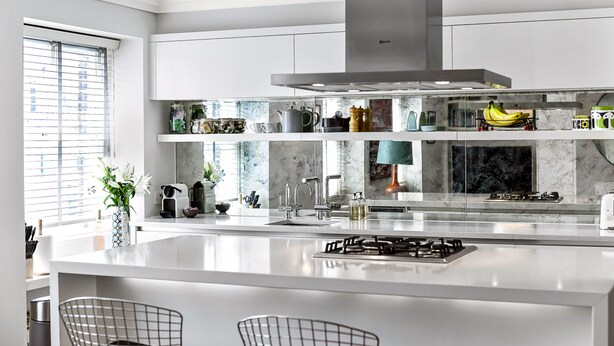 A modern kitchen with white cabinetry, a central island with a gas stove, and a variety of kitchen appliances and decorations on the shelves.