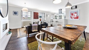 A modern kitchen with a wooden table, pendant lights, and a view to the dining area.