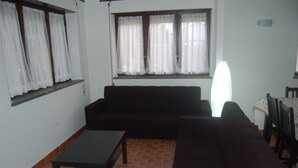 Ein Wohnzimmer mit einem dunkelbraunen Sofa, einem kleinen schwarzen Tisch und einem Fenster mit weißen Vorhängen.