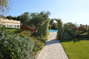 A stone pathway leading to a pool area surrounded by lush greenery and flowering plants. - Villa Collebelvedere - Apartment East - Home Restaurant (Fara Sabina)