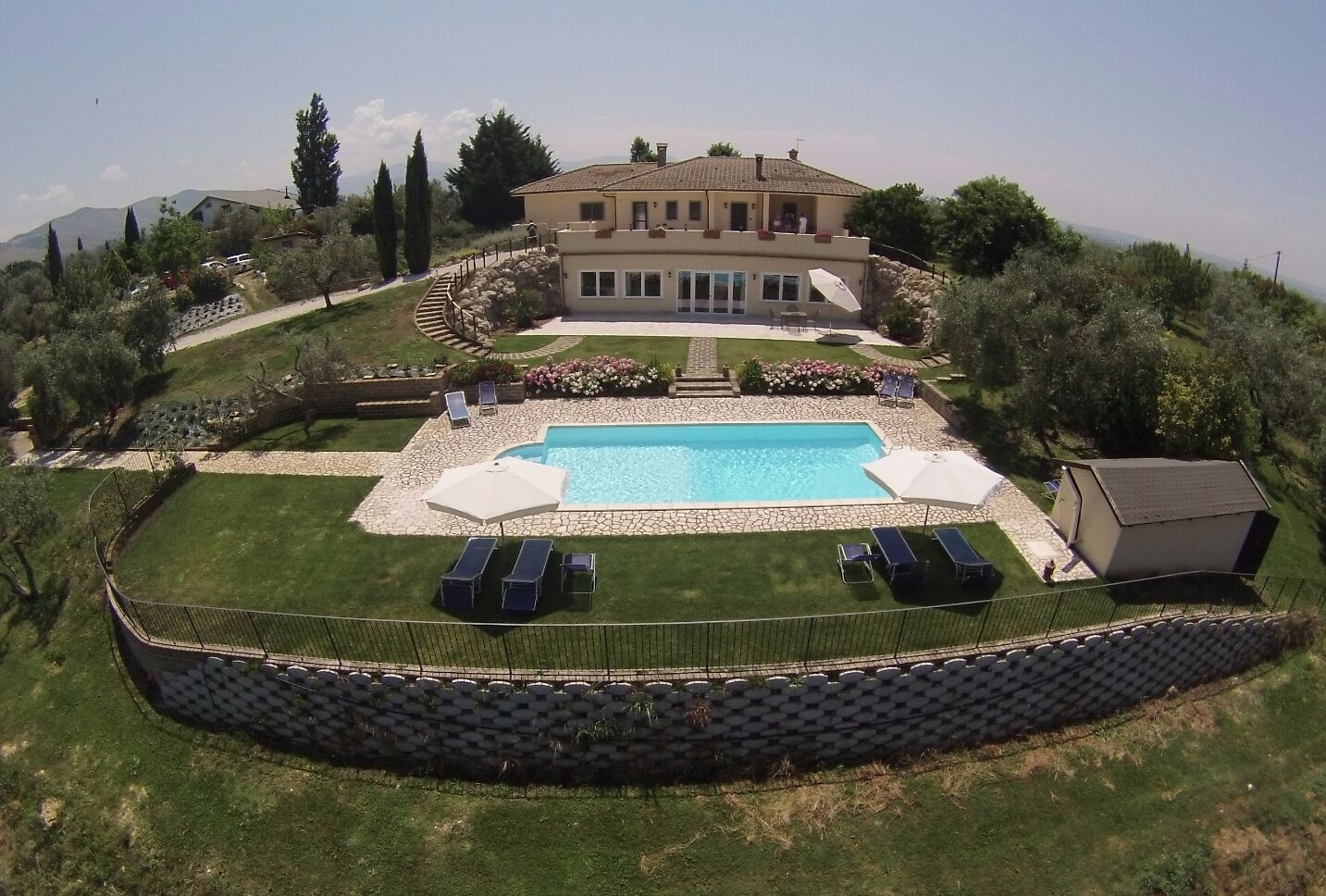 Une grande maison avec une piscine, entourée d’une pelouse bien entretenue et d’un mur de pierres.
