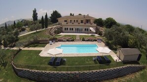 Ett stort hus med en swimmingpool, omgivet av en välskött gräsmatta och en mur av sten.