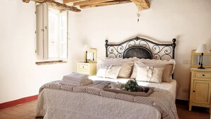 A bedroom with a bed, bedside tables, a window, and a wooden ceiling beam. - Tuscan rustic house with exclusive private garden (Montemagno)