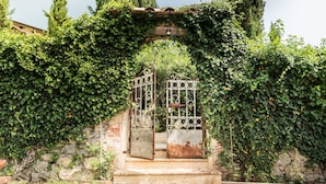 An arched entrance with a metal gate, surrounded by lush green ivy, leading to a stone building. - Tuscan rustic house with exclusive private garden (Montemagno)