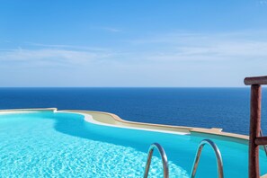 Céu azul e vista para o oceano a partir de uma área com piscina e guarda-corpo de madeira.
