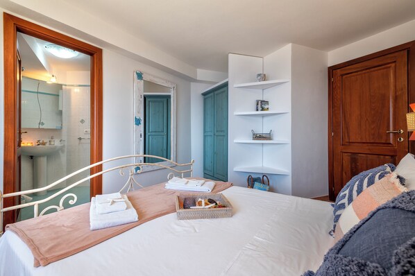 Quarto com uma cama, mesa de cabeceira com toalhas, pequeno cesto e porta de madeira.
