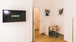 A room with a flat-screen TV displaying 'android', a desk, a chair, and two artworks on the wall.