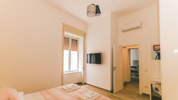 A bedroom with a bed, a TV mounted on the wall, and an air conditioning unit.