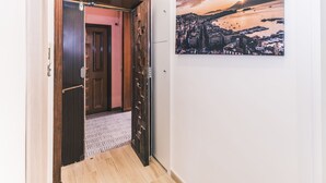 A hallway with a wooden door, a patterned rug, and a cityscape painting on the wall.