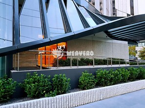 A modern building with a unique curved roof structure, a visible entrance with glass doors, and a landscaped area with neatly trimmed bushes. - Modern Living in Southbank Apartments (Southbank)