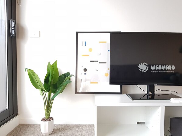 A modern room with a flat-screen TV on a white stand, a potted plant, and a door with a black frame. - Modern Living in Southbank Apartments (Southbank)