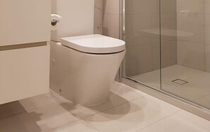 A modern bathroom with a toilet, a glass shower enclosure, and a tiled floor. - Modern Living in Southbank Apartments (Southbank)