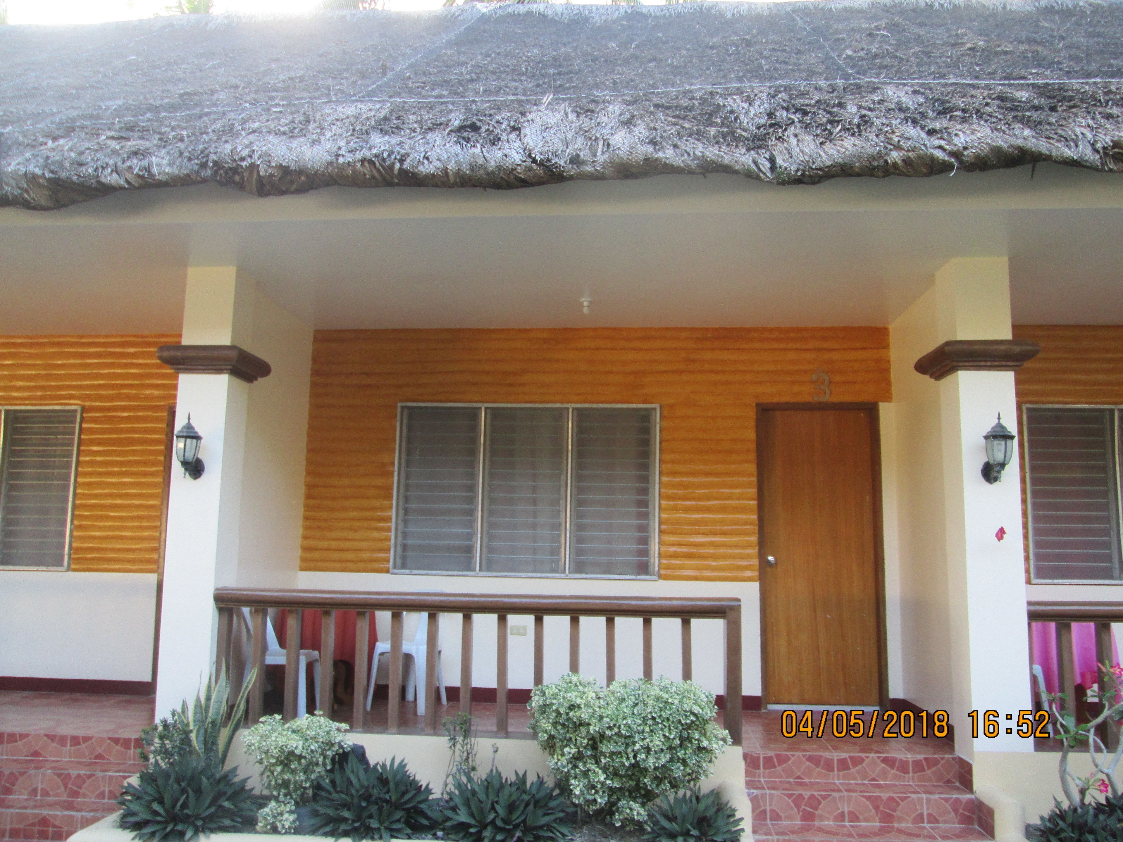 A building with a thatched roof, wooden doors, and windows with blinds. There are potted plants in front.