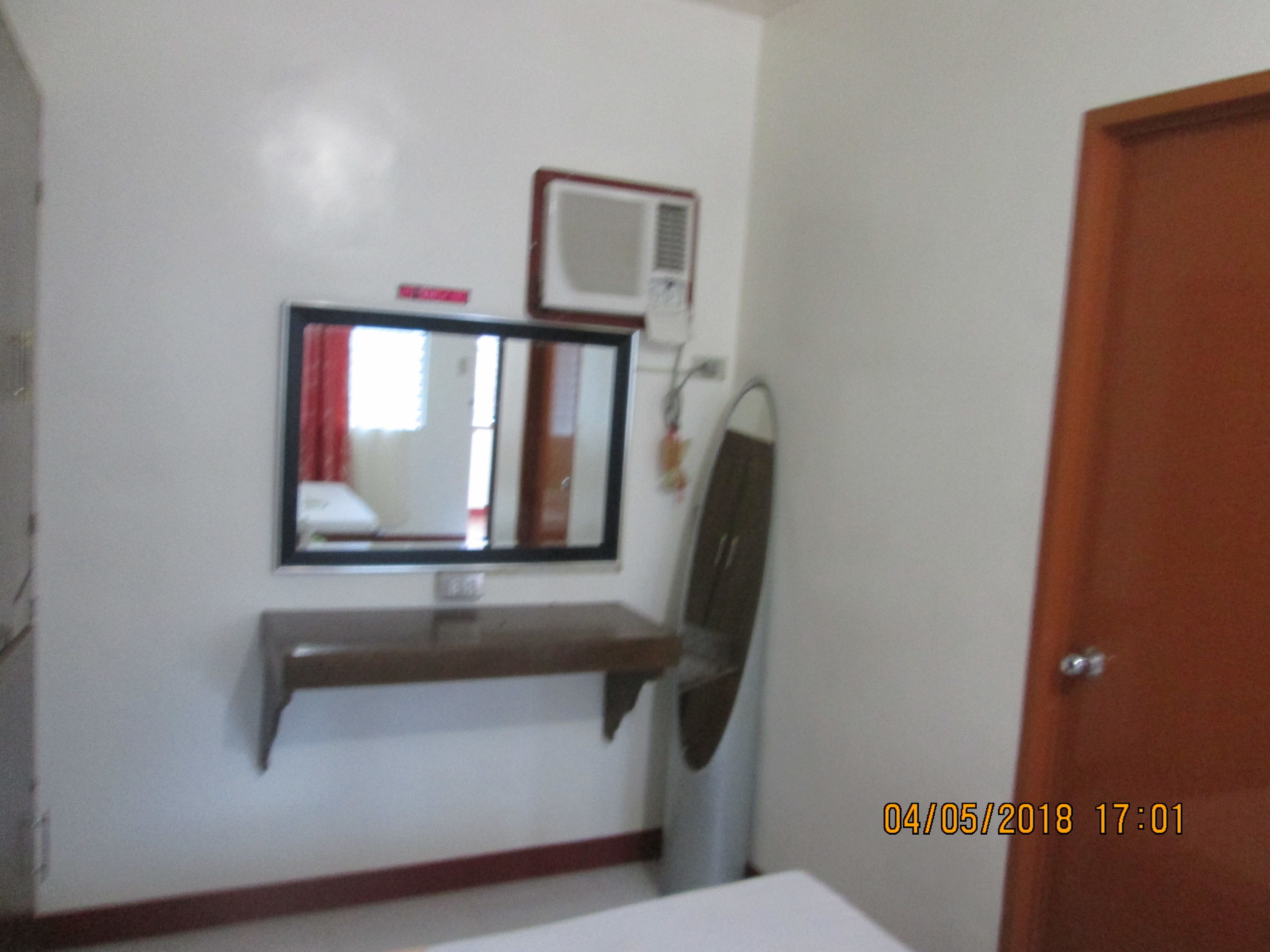 A room with a white wall, a mounted air conditioner, a mirror, and a wooden shelf.
