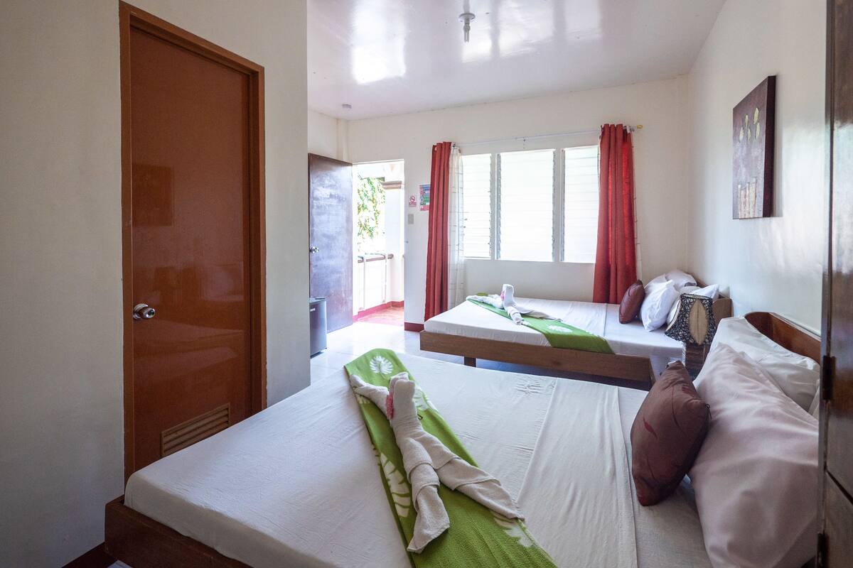 Ett hotellrum med två sängar, en trädörr och ett fönster med röda gardiner.