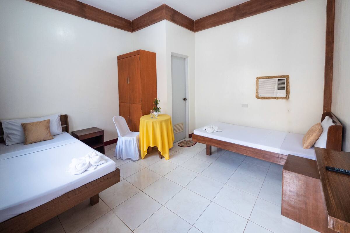 Ett hotellrum med två sängar, en garderob i trä, ett litet bord med en gul duk och en väggmonterad luftkonditioneringsanläggning.