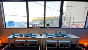 Un coin repas avec une table dressée pour quatre personnes, des chaises et une vue sur l’océan grâce à de grandes fenêtres.
