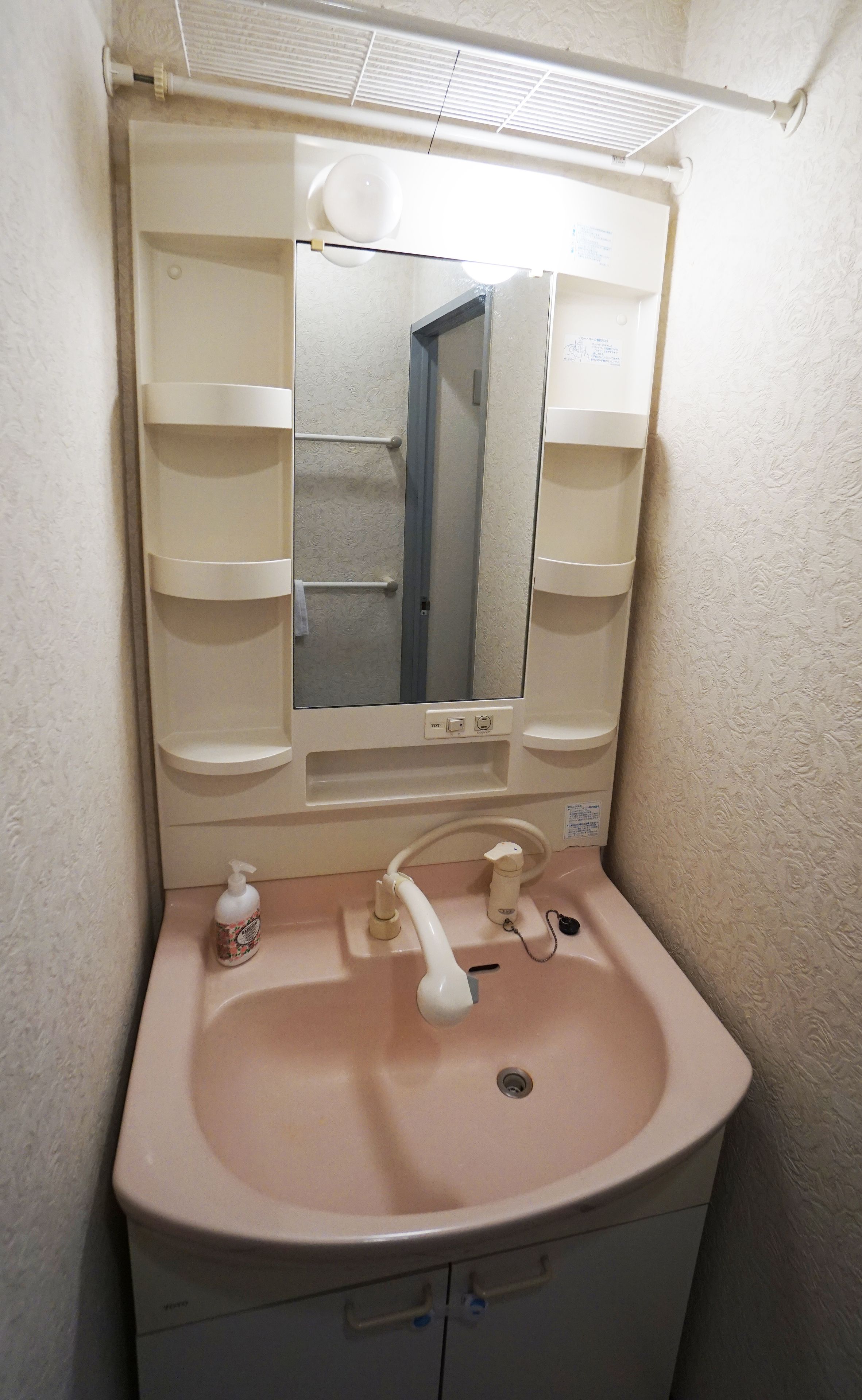 Un baño con un lavamanos rosa, un espejo y un perchero para toallas.