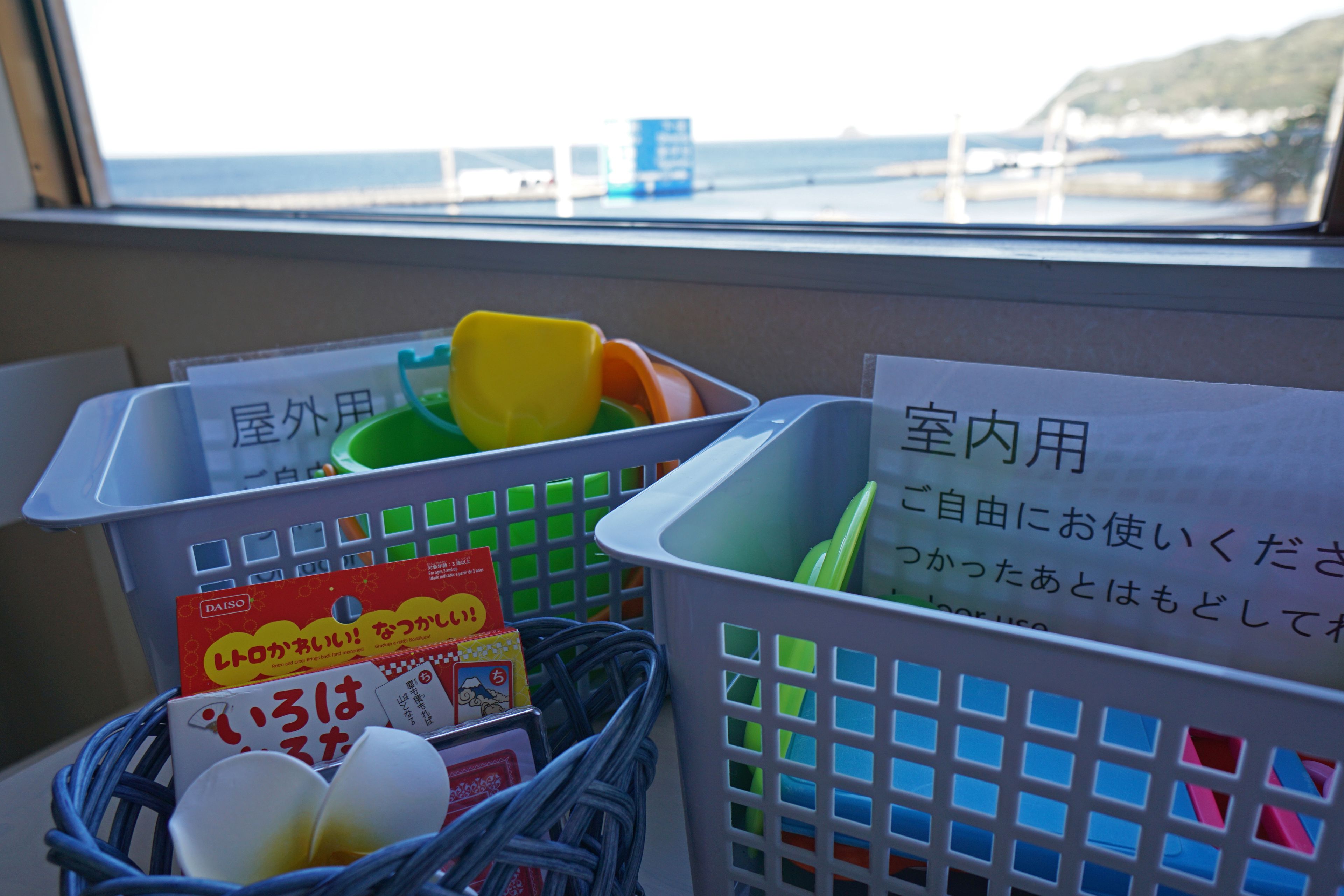 A view of a room with a window overlooking a coastal area, featuring laundry baskets and a basket with a card.