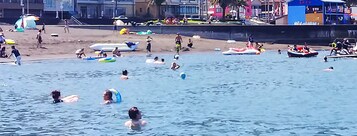 Una playa concurrida, gente nadando y usando distintos juguetes acuáticos.
