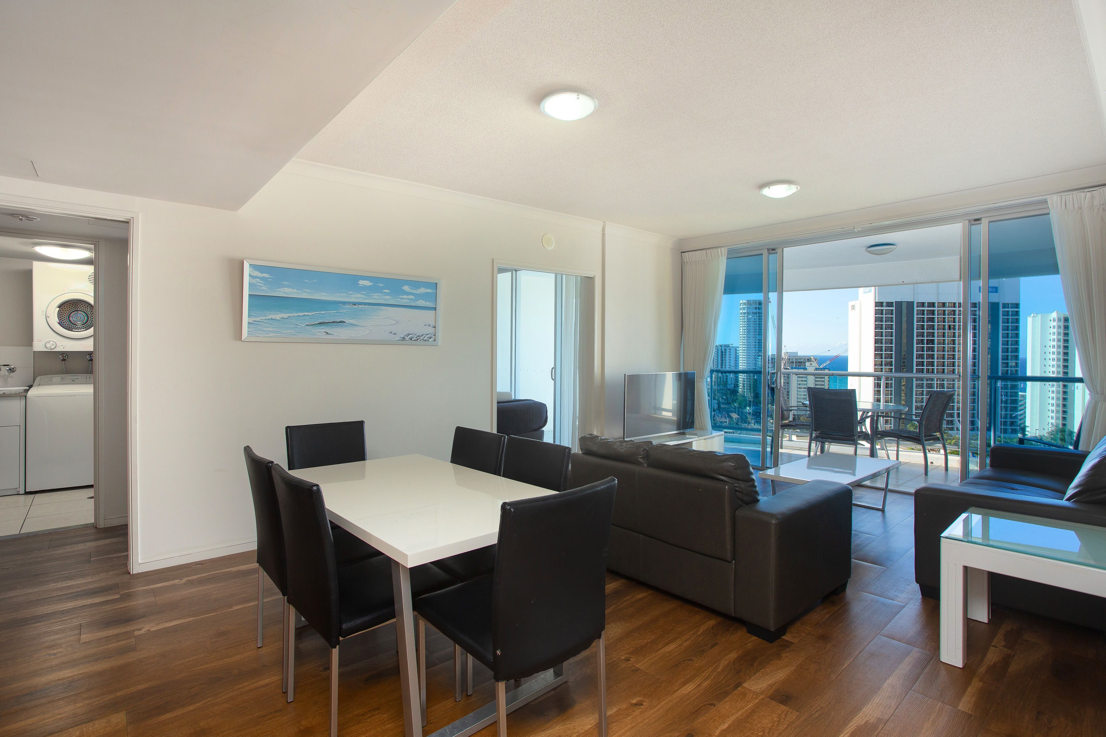Un salon moderne comprenant un coin repas, un canapé, un téléviseur et un balcon offrant une vue sur la ville.