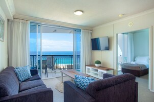 Una habitación de hotel moderna con balcón, un conjunto de sofás, una mesita y una cama.