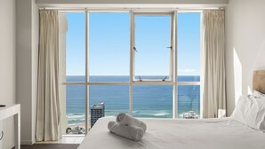 Habitación de hotel con un ventanal amplio que ofrece vistas al océano y un edificio al otro lado del agua.