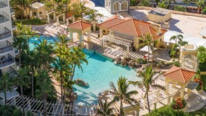 Un resort con piscina central, varias zonas de descanso y un edificio de techo con tejas.