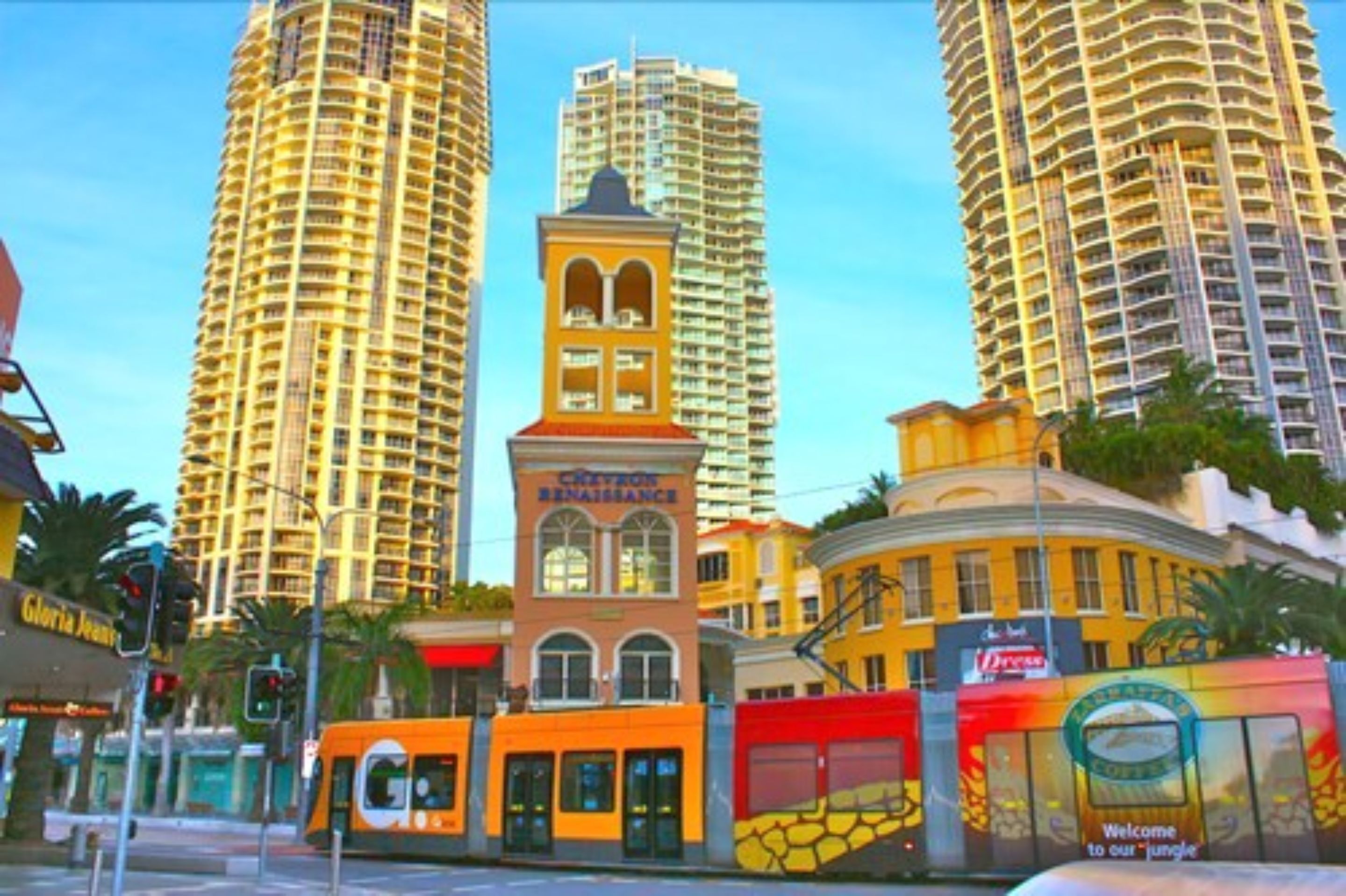 Paisagem urbana com edifícios altos, um edifício amarelo de destaque com torre de relógio e um ponto de ônibus com o logotipo 'G'.