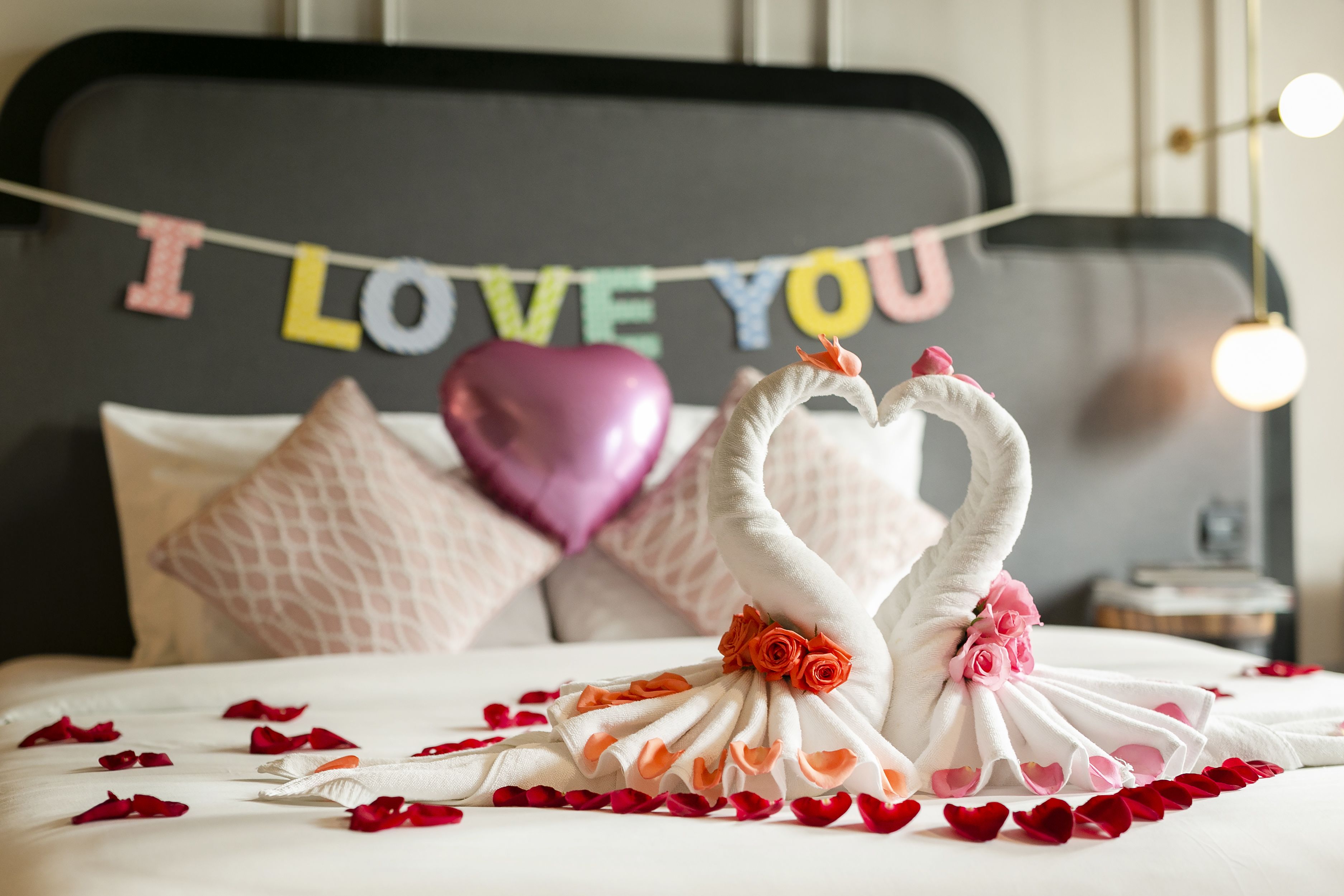 Una cama con una toalla dispuesta en forma de corazón, un cartel que dice 'I LOVE YOU' y un adorno en forma de corazón rosa.