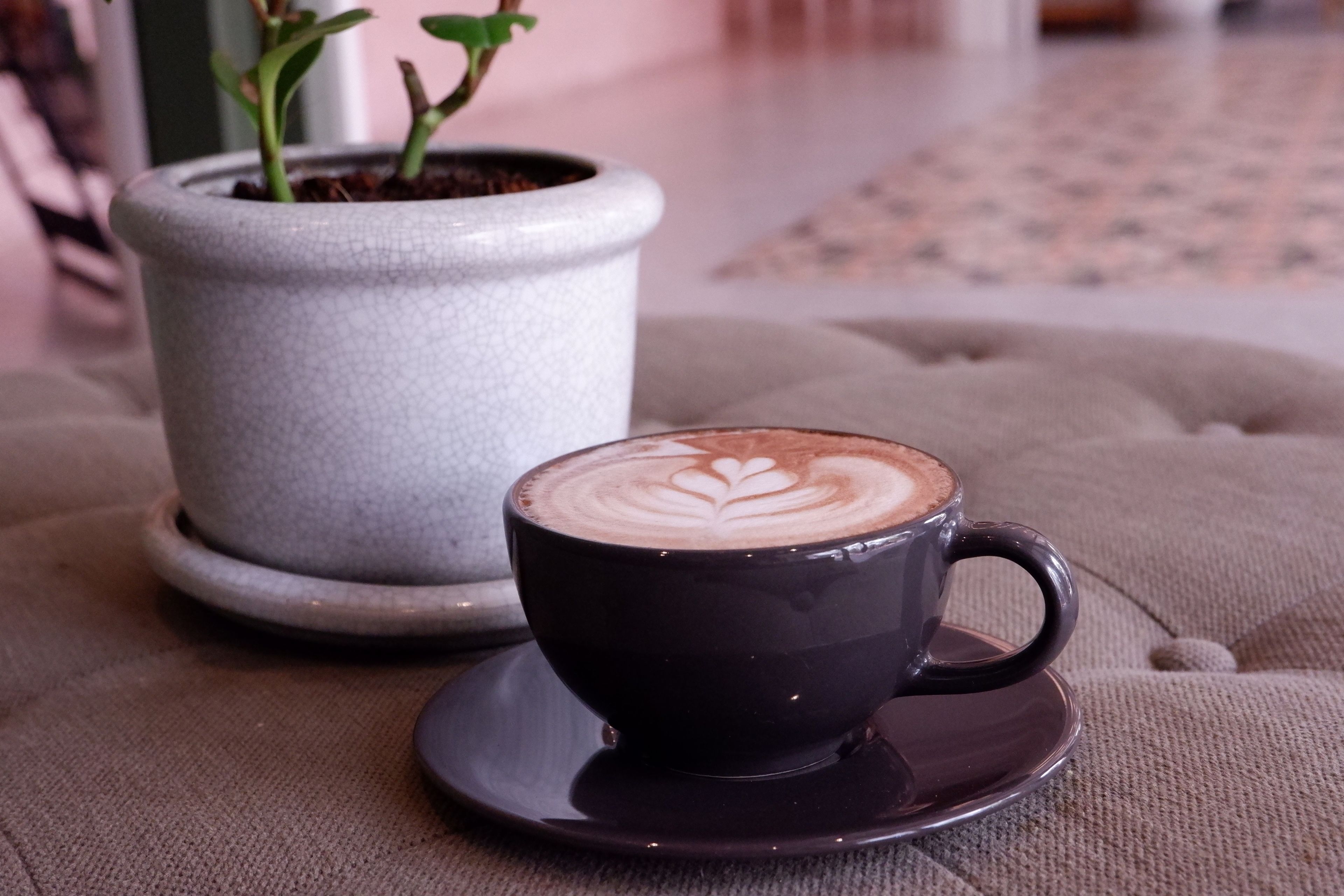 En sort kop kaffe med latte kunst på en bakke, placeret på en struktureret overflade.