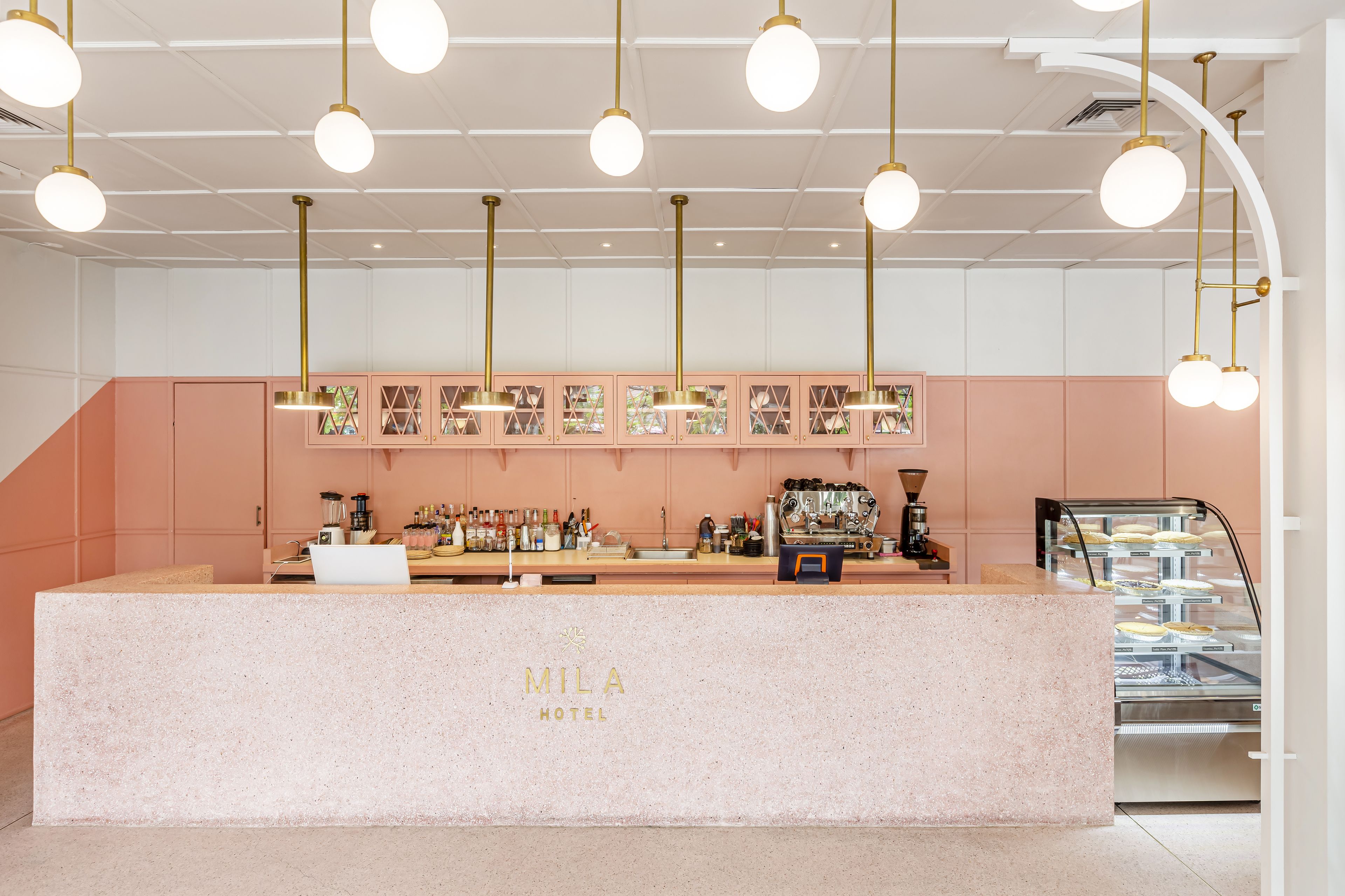 Zona de recepció d'hotel amb un taulell de marbre, una màquina de cafè i una vitrina amb pastissos.
