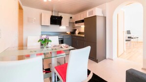 A modern kitchen with a glass dining table, white chairs, and a refrigerator.
