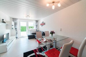 A modern living room with a glass dining table, white walls, and a view to the outside.